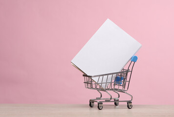 Mini supermarket cart with white cover book mockup on pink background © splitov27