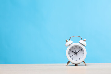 White alarm clock on table, blue background