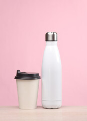 White thermos bottle and paper coffee cup on the table, pink background