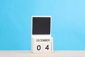 White wooden block monthly calendar with the date december 4 on the table, blue background. Planning, deadline