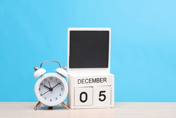 White wooden block monthly calendar with the date december 5 and alarm clock on the table, blue...