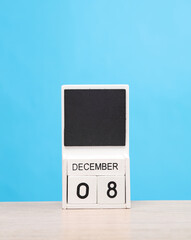 White wooden block monthly calendar with the date december 8 on the table, blue background. Planning, deadline