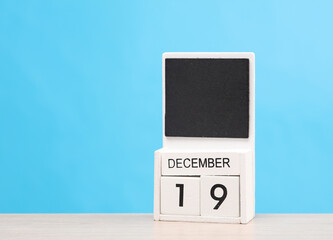 White wooden block monthly calendar with the date december 19 on the table, blue background. Planning, deadline