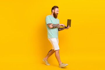 Full size profile portrait of nice positive man use netbook walking isolated on yellow color background