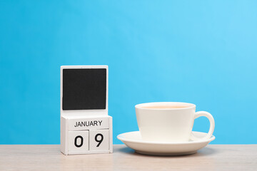 White wooden block monthly calendar with the date january 09 and coffee cup on the table, blue background. Planning, deadline
