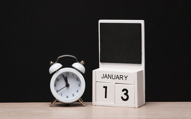 White wooden block monthly calendar with the date january 13 and alarm clock on the table, black blackbackground. Planning