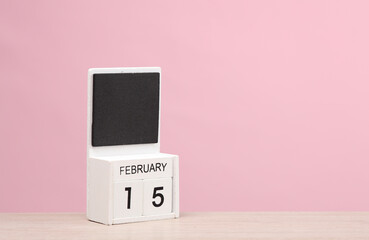 White wooden block monthly calendar with the date february 15 on the table, pink background. Planning, business concept