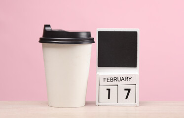 White wooden block monthly calendar with the date february 17 and coffee cup on the table, pink...