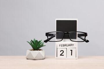 White wooden block monthly calendar with the date february 21 and eyeglasses, plant on the table, gray background. Planning, business concept