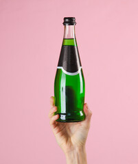 Female hand holding bottle of green Irish beer on pink background