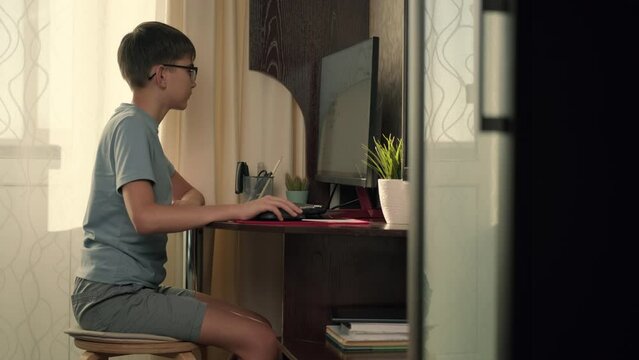 A boy solves interactive exercises using a computer at home while sitting at a table.Authentic Action,Home Window,Sun Flare,Bright Light