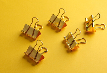 Golden paper binder clips on yellow background