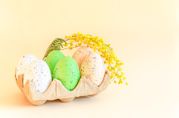 colorful Easter eggs in ecological packaging and mimosa flower on beige background. happy Easter