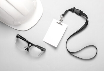 Empty white ID card badge with a protective construction helmet and protective glasses on a gray...