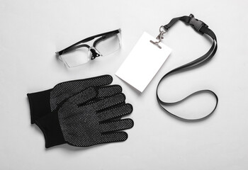 Empty white ID card badge with protective glasses and gloves on a gray background. Engineer,...