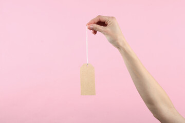 Craft empty price tag on a string in a female hand, pink background