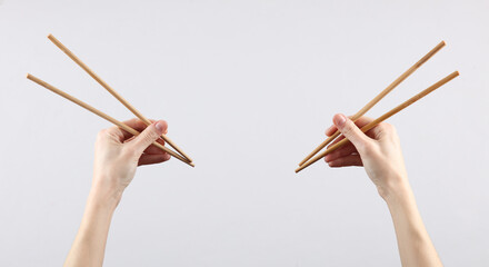 Two pairs of Chinese chopsticks in female hands on a gray background