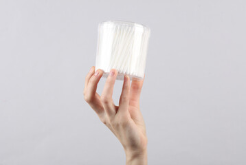 Hand holds box of ear cotton buds on gray background