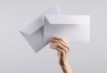 female hand holds two white envelopes on a gray background