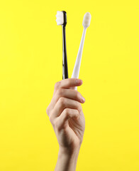 Female hand holding white and black toothbrushes on yellow background