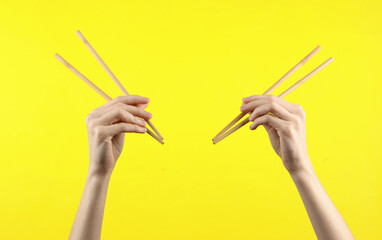 Two pairs of Chinese chopsticks in female hands on yellow background