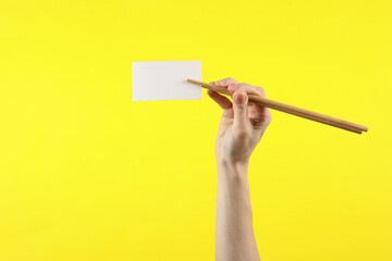 Chinese chopsticks with white business card in a female hand on yellow background