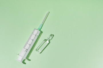 Transparent ampoule with medicine and syringe on green isolated background. Vaccination or beauty therapy concept. A place for your design or text. World Health Day.