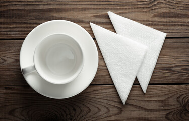 Empty white ceramic cup with saucer and napkins top view on wooden table