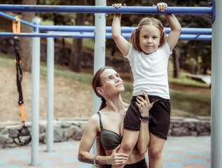 Obraz premium Young athletic mom will walk her daughter to train on the training ground. Active family. Physical Education