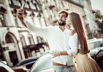 Naklejka premium Young couple in love makes selfie on smartphone in the city. Romantic love concept