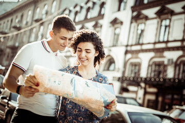 Young smiling couple of tourists exploring the city map in the European city. Travel concept
