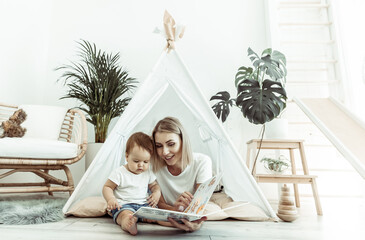 Happy woman mom and her little daughter read book in wigwam at home © splitov27
