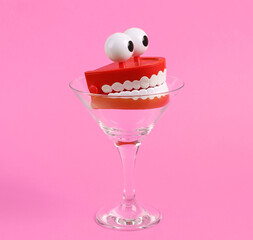 Toy jaw in cocktail glass on pink background. Fresh idea. Minimal party concept, creative layout