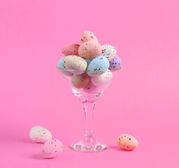 Cocktail glass with colored eggs on pink background. Creative idea. Minimal Easter concept. Concept art, layout