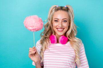 Photo of cheerful funky girl hold puffy cotton candy stick headphones hang neck isolated on teal...