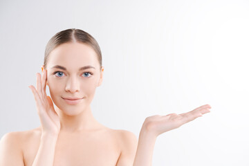 Beauty spa with perfect skin portrait. Beautiful Brunette Spa Girl showing blank copy space on open hand for text. Product offer. Gestures for advertising. Light background in the studio