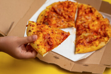 hand taking a slice of pizza from a cardboard pizza box