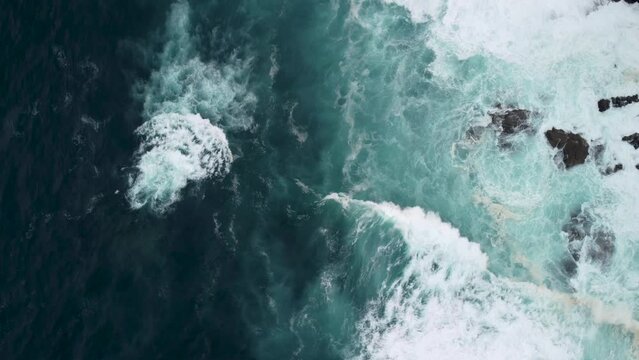 Drone Rotating Over Powerful Waves Crashing On Rocky Coastline With Foamy Surfaces. Aerial Shot