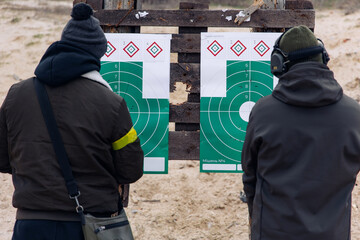 Two shooters examine their targets with shot through holes at a training shooting range.