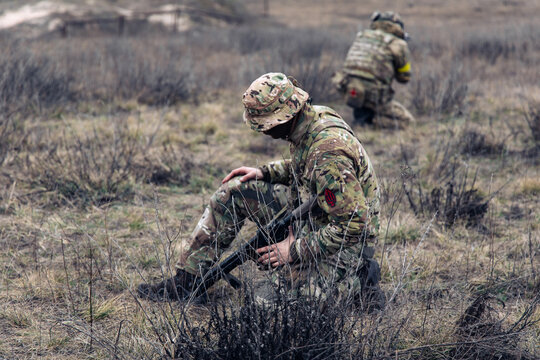 Two armed Ukrainian soldiers sit and rest in steppe against background of dry grass.