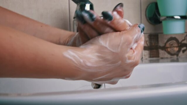 Girl washes her hands with soap under the tap close-up. Hand hygiene from bacteria. Foam lathers in female hands. Soap kills harmful bacteria. Cleanliness.