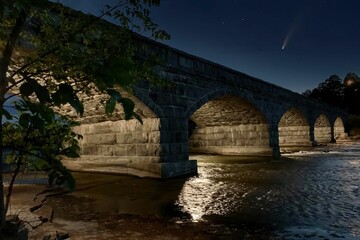 Low angle view of a stone bridge with a Comet visible passing in the sky during the night