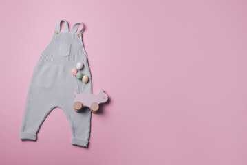 Yellow mustard color baby romper , soft rainbow, car toy, silicone pyramid, cubes for newborn on pink background. Gender neutral baby stuff and accessories. Flat lay, top view. Copy space