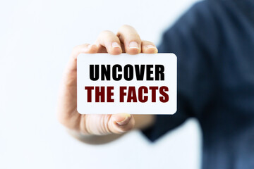 Uncover the facts text on blank business card being held by a woman's hand with blurred background. Business concept about uncover the facts.