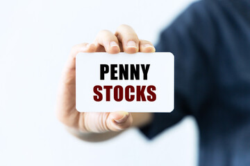 Penny stocks text on blank business card being held by a woman's hand with blurred background. Business concept about penny stocks.
