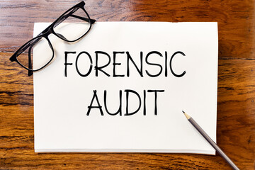 Forensic audit handwriting text on blank notebook paper on wooden table with pencil and glasses aside. Business concept and legal concept about forensic audit.