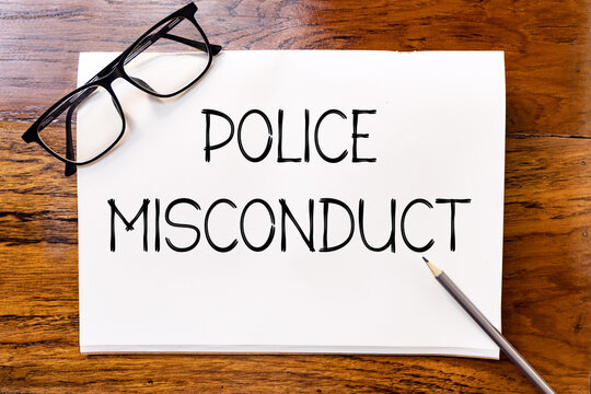 Police misconduct handwriting text on blank notebook paper on wooden table with pencil and glasses aside. Business concept and legal concept about police misconduct.
