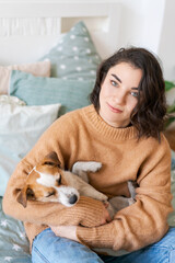 Woman hugs cute little dog lying in her arms at home. Close-up. Trust and calmness, care, friendship and love. Happy cozy moments of life. Stay at home concept, animal family member