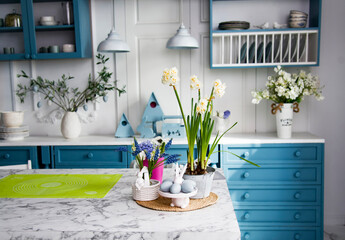 flowers in a vase on the table in the white and blue kitchen with easter decoration