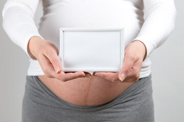 A pregnant girl holds an empty frame. Stub for text. Copy space.
